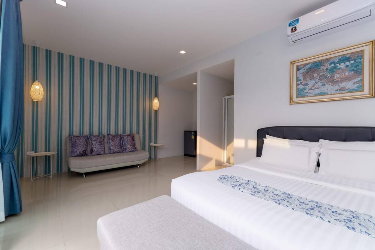 Una habitación de hotel moderna con una cama grande, un sofá, una mesita y un cuadro en la pared.