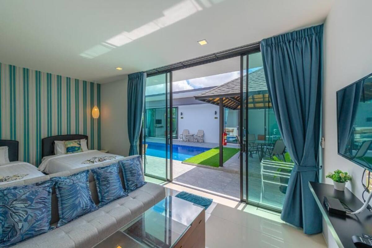 Habitación de hotel con cama, sofá, televisión y puerta de vidrio que da a una zona de piscina.