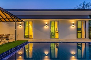 Ein modernes Haus mit Swimmingpool, Glastüren und Außenbeleuchtung.