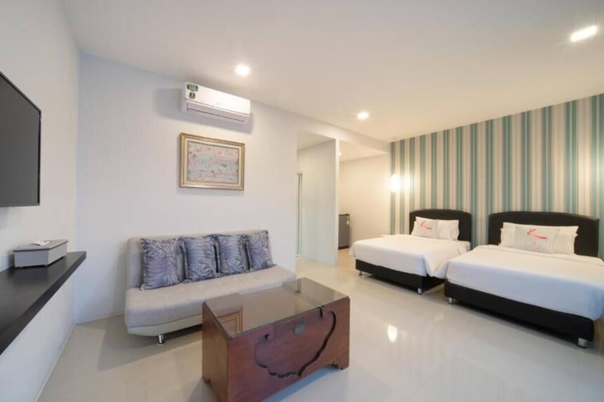 Una habitación de hotel moderna con una televisión de pantalla plana, un sofá, dos camas, una mesita de café y papel tapiz a rayas.