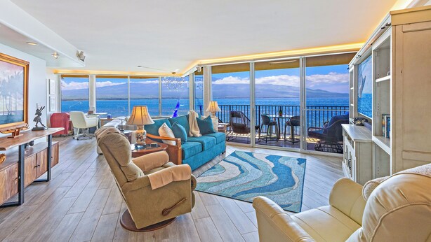 A spacious living area with a large window overlooking the sea, a sofa, a chair, a desk, and a bookshelf. - Celebrate Honeymoon, Anniversary or Birthday...Panoramic Ocean View! (Wailuku)