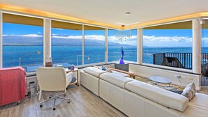 A modern living room with a large window, a sofa, a small table, and a chair. - Celebrate Honeymoon, Anniversary or Birthday...Panoramic Ocean View! (Wailuku)