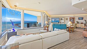 A modern living room with a large window, a sofa, a dining area, and a view of the sea. - Celebrate Honeymoon, Anniversary or Birthday...Panoramic Ocean View! (Wailuku)