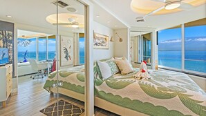 A modern bedroom with a large bed, a desk, and a view of the ocean. - Celebrate Honeymoon, Anniversary or Birthday...Panoramic Ocean View! (Wailuku)