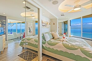 A modern bedroom with a large bed, a desk, and a view of the ocean. - Celebrate Honeymoon, Anniversary or Birthday...Panoramic Ocean View! (Wailuku)