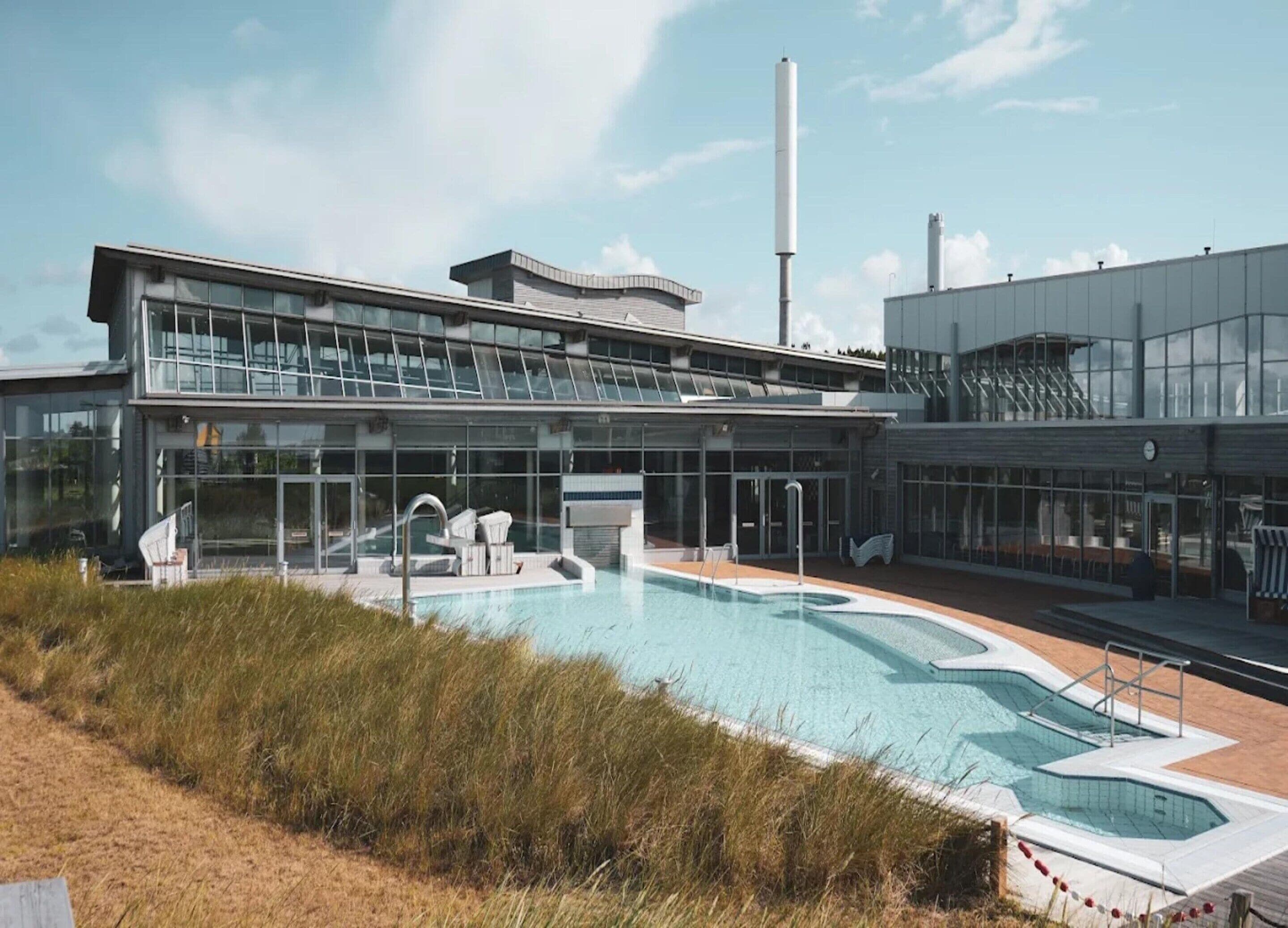 A modern building with a large pool area, including a hot tub and lounge chairs.