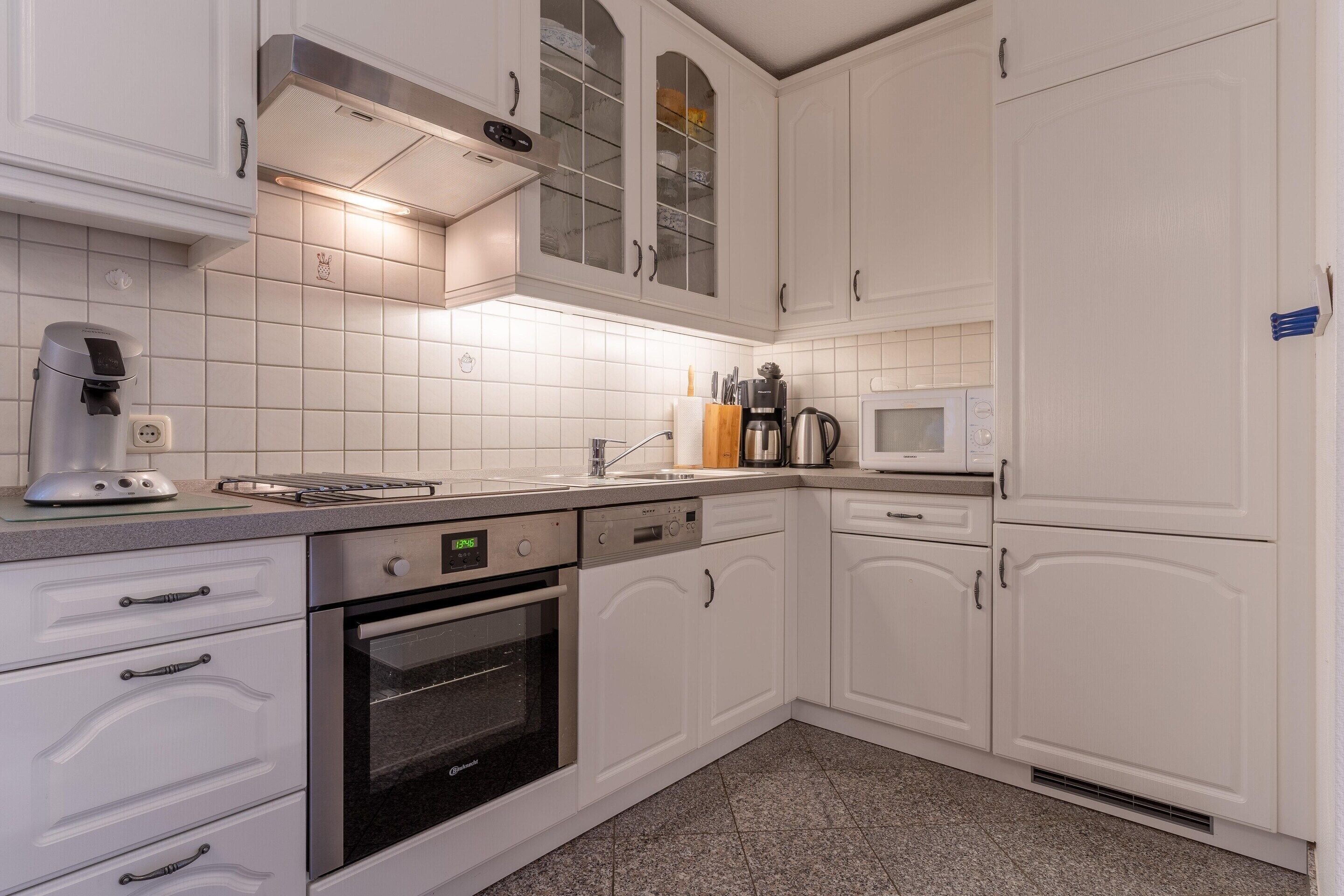 A modern kitchen with white cabinetry, a built-in oven, a coffee maker, and a microwave.