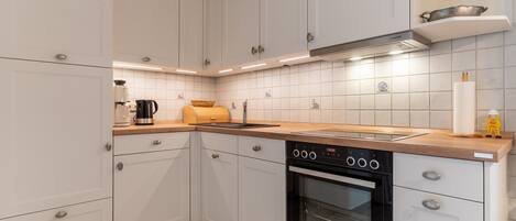 A modern kitchen with white cabinets, a black oven, and a wooden countertop.