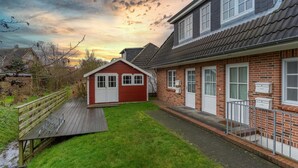 A residential property with a red house, a wooden deck, and a brick exterior. - Ferienwohnung fur 2 in St. Peter-ording (St. Peter-Ording)