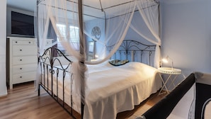 A four-poster canopy bed with a white bedspread, a bedside table with a lamp, and a small round table with a lamp. - Ferienwohnung in Busum (Büsum)