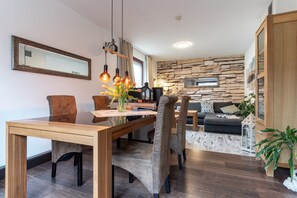 A modern living space with a dining area, a stone wall, and a wooden cabinet. - Ferienwohnung in Busum (Büsum)
