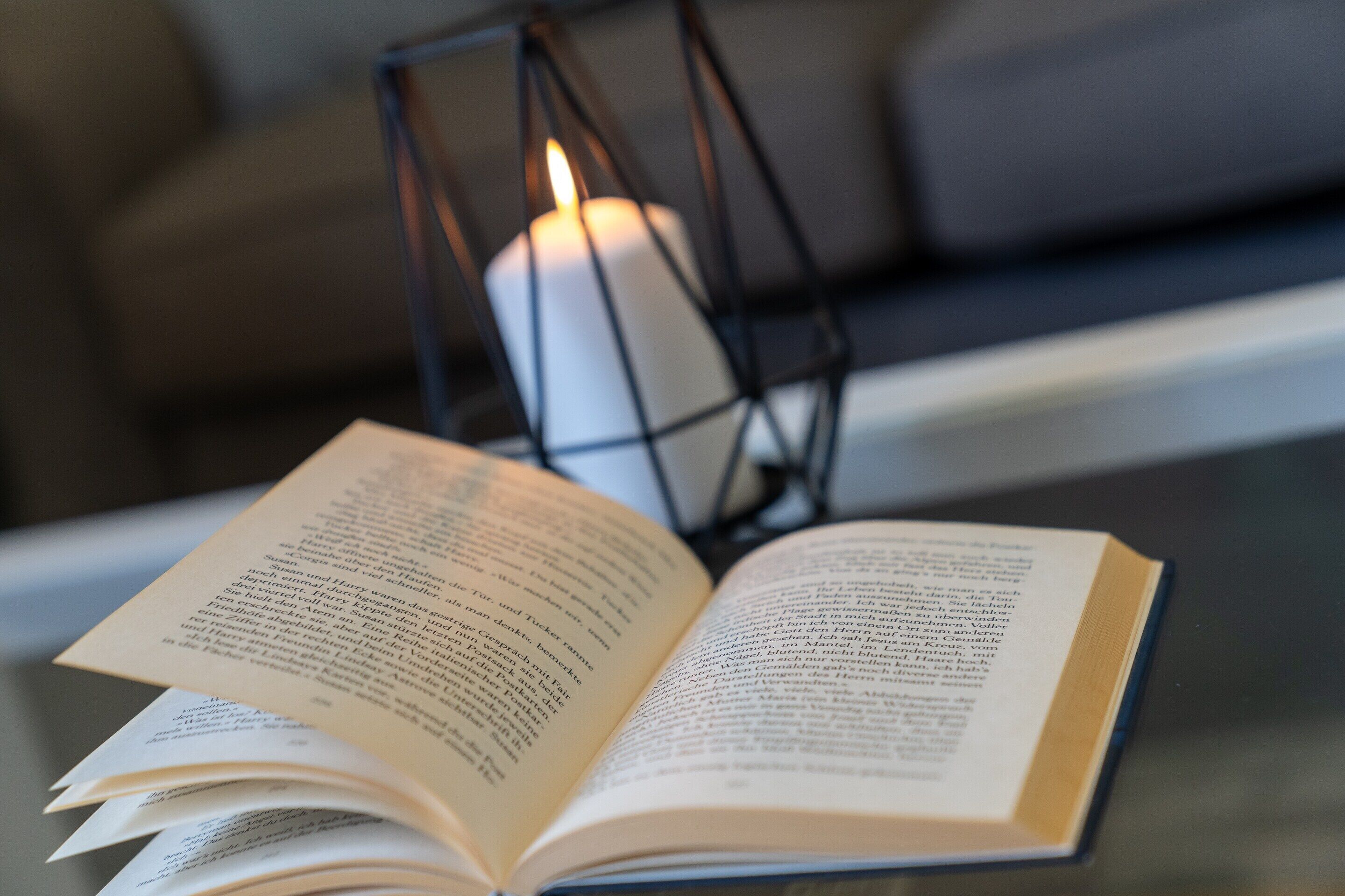 Een open boek op een tafel, met een brandende kaars in een draadhouder op de achtergrond.