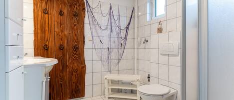 A bathroom with a wooden door, a white sink, a toilet, and a shower area.