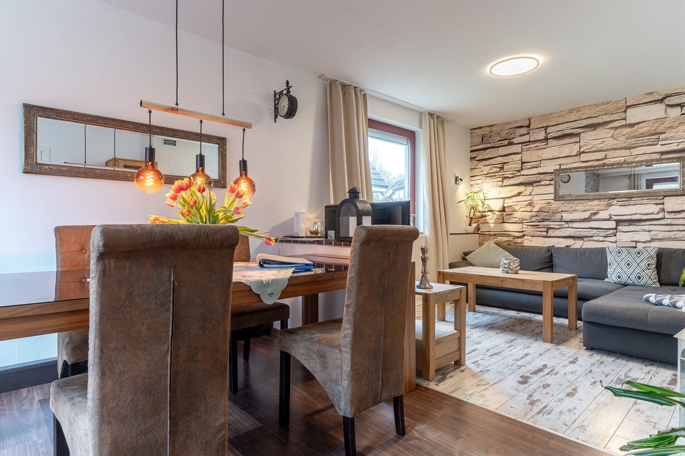 A modern living room with a dining area, stone wall, and large windows.