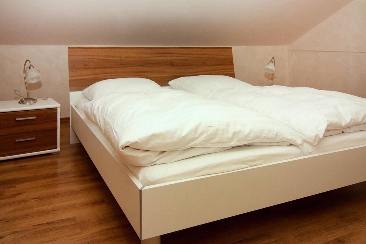Ein ordentlich bezogenes Bett mit weißen Leinen in einem Zimmer mit Holzboden und einem hölzernen Kopfstück.