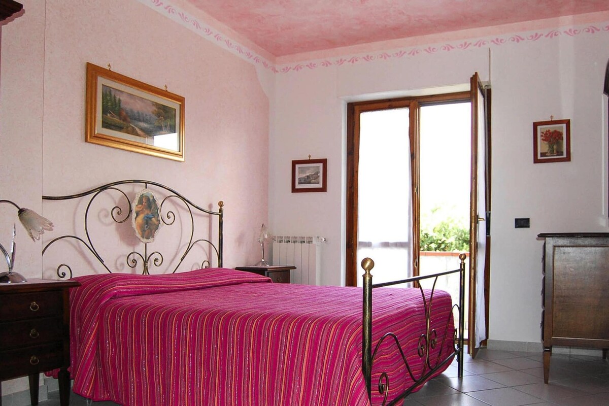 Ein Schlafzimmer mit Bett, Nachttisch, Kommode, Fenster und Tür.