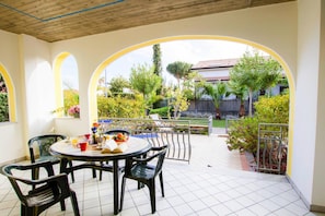 An outdoor patio with a round table and chairs, surrounded by arches and a view of a garden and buildings. - Apartment in Cilento Near Sandy Beach (Ascea)