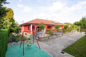 Ein rotes Gebäude mit Spielplatz, überdachter Terrasse und gepflegtem Rasen.