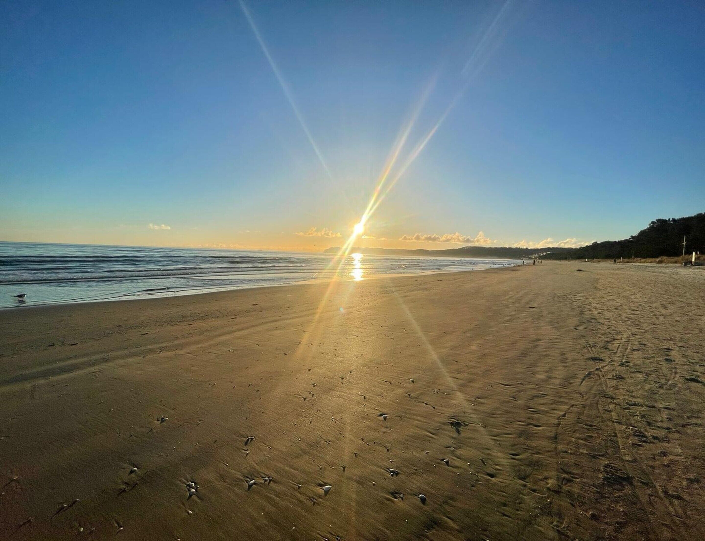 Een strand met een heldere lucht en de zon laag aan de horizon, waardoor het zand helder verlicht wordt.