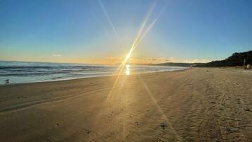 Een strand met een heldere lucht en de zon laag aan de horizon, waardoor het zand helder verlicht wordt.
