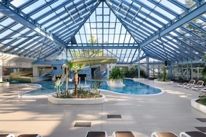 En indendørs swimmingpool med glasloft, liggestole og en vandrutsjebane.