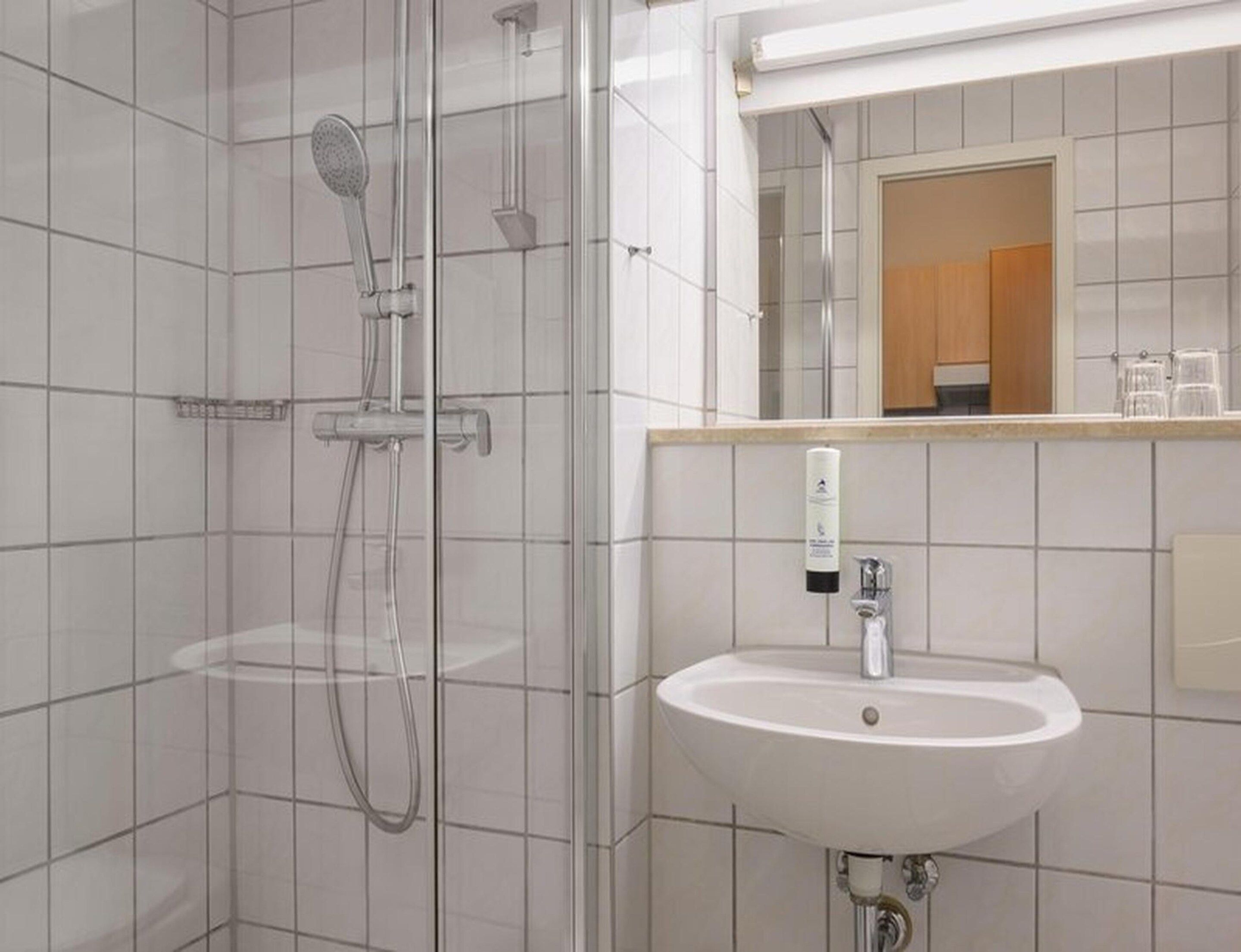 Ein modernes Badezimmer mit einer gläsernen Duschkabine, einem weißen Waschbecken und einem Spiegel darüber.