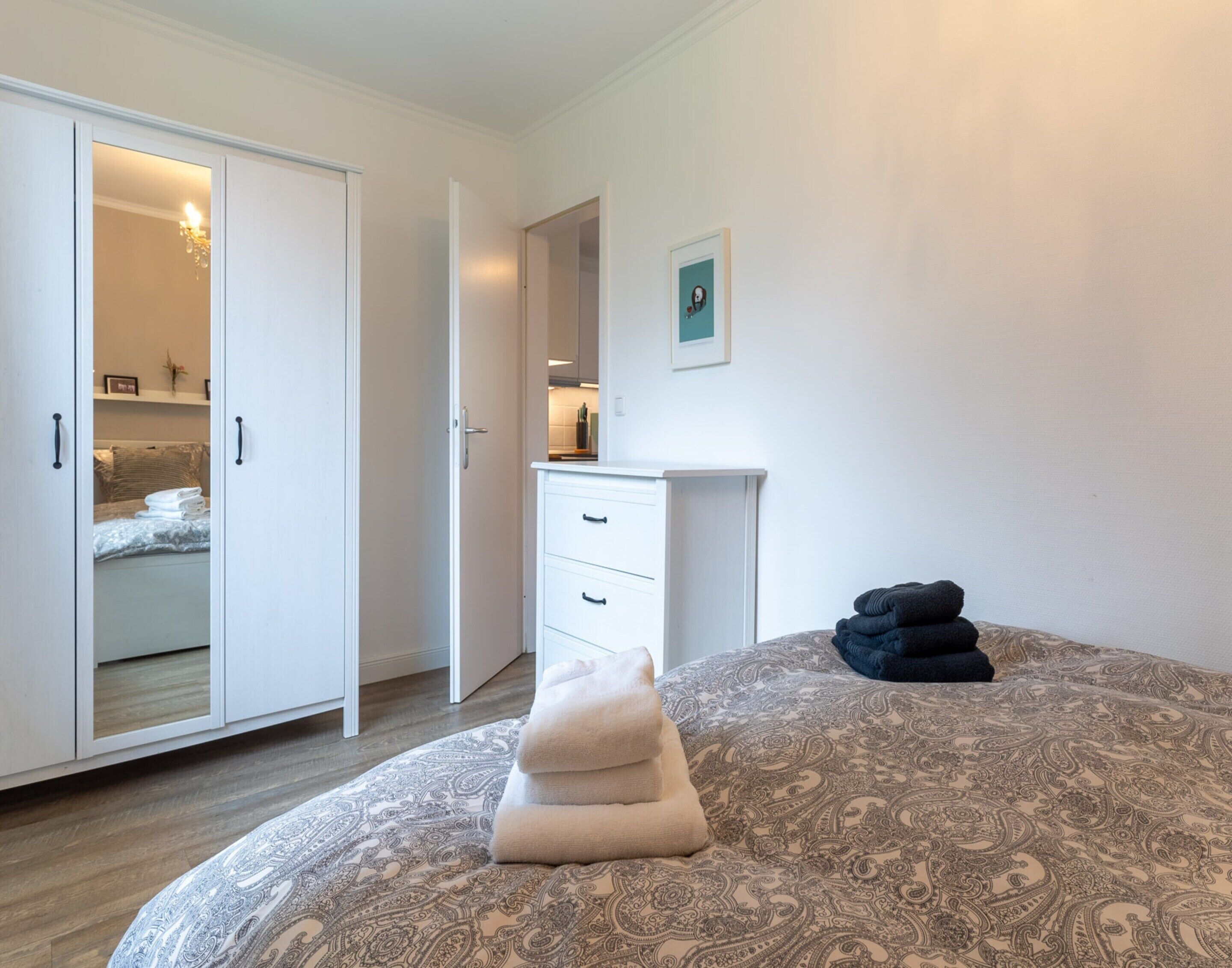 A bedroom with a bed, a bedside table, a wardrobe, and an open door leading to a bathroom.