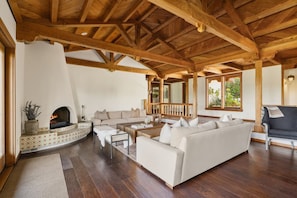 Un salón espacioso con chimenea, vigas de madera, un sofá y vistas a zonas verdes.
