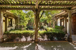 Un jardín cubierto con una estructura de pérgola, rodeado de abundante vegetación y diversas plantas.