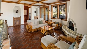 A spacious living area with a stone floor, wooden beams, a fireplace, and wicker furniture.