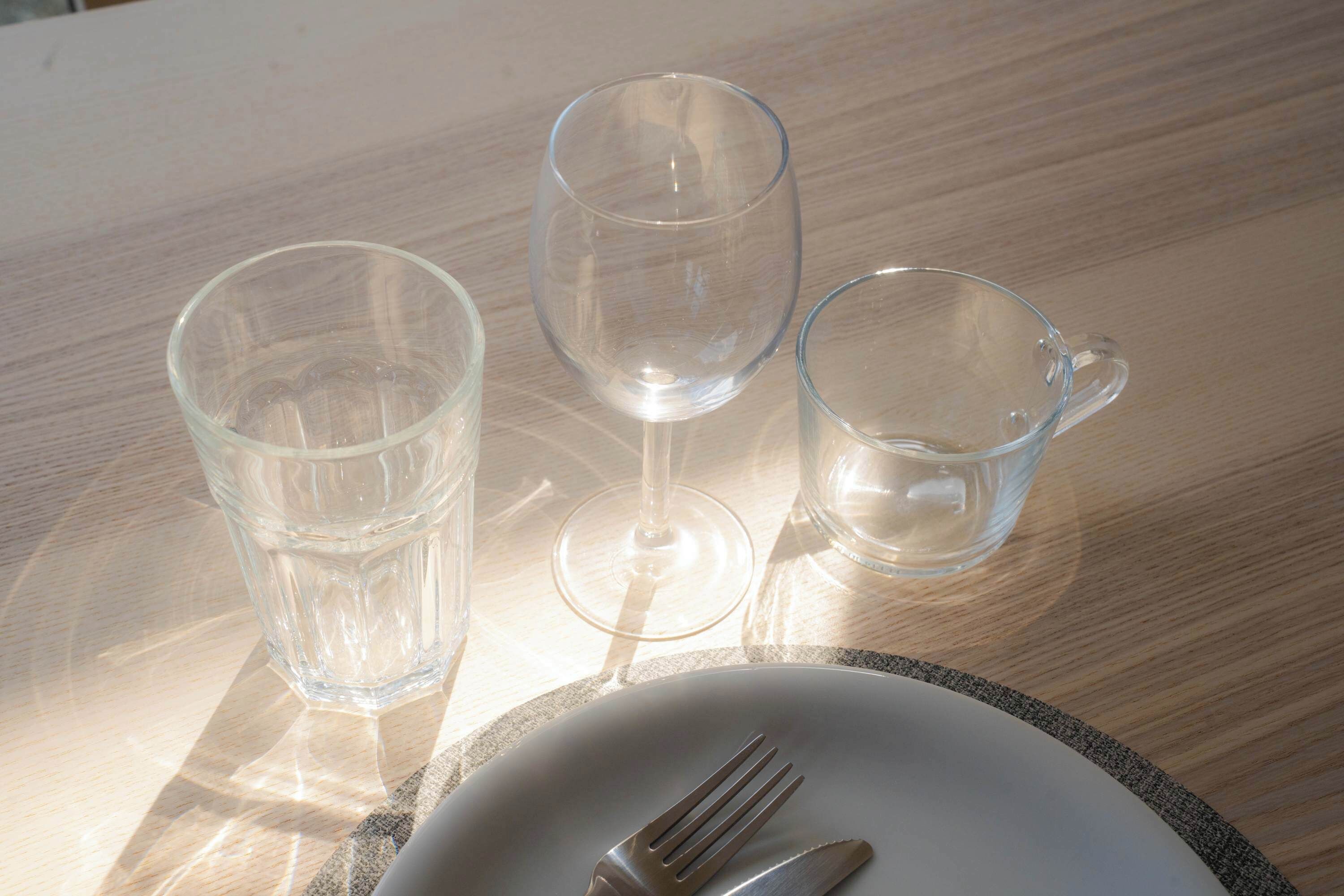 A dining table with a plate, fork, and three clear glasses.