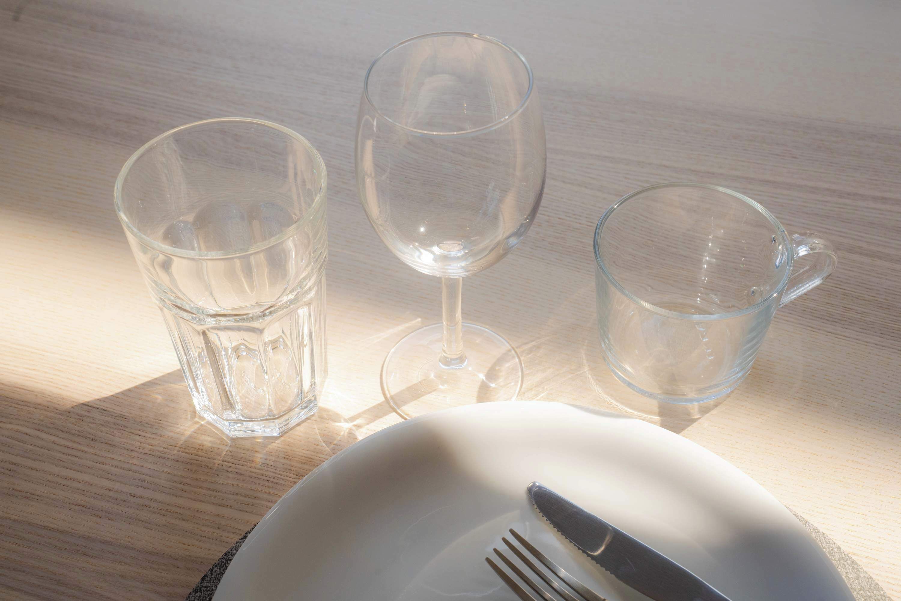 A table with a white plate, a knife, and three clear glasses.