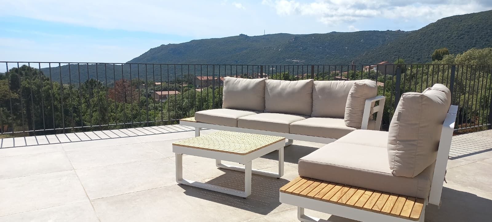 Une terrasse extérieure avec un canapé et une table, une rambarde en métal et un paysage montagneux en arrière-plan.