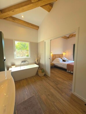 A modern bathroom with a freestanding bathtub, a window, and a wooden floor.