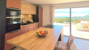A modern kitchen with a wooden island, a dining area with a bench, and a view of the outdoors. - Villa with pool, sea view, Corse-du-Sud (Monacia-d'Aullène)