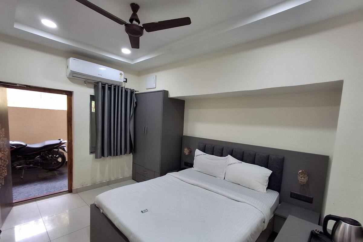 A modern hotel room with a bed, a wardrobe, a ceiling fan, an air conditioning unit, and a motorcycle outside.