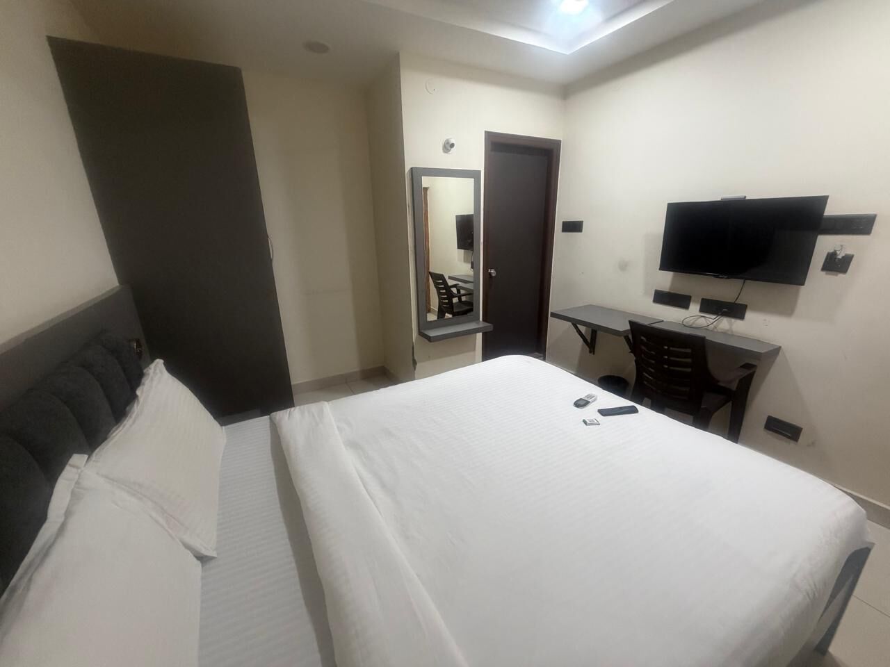 Habitación de hotel con cama, escritorio, silla, televisor de pantalla plana y espejo.