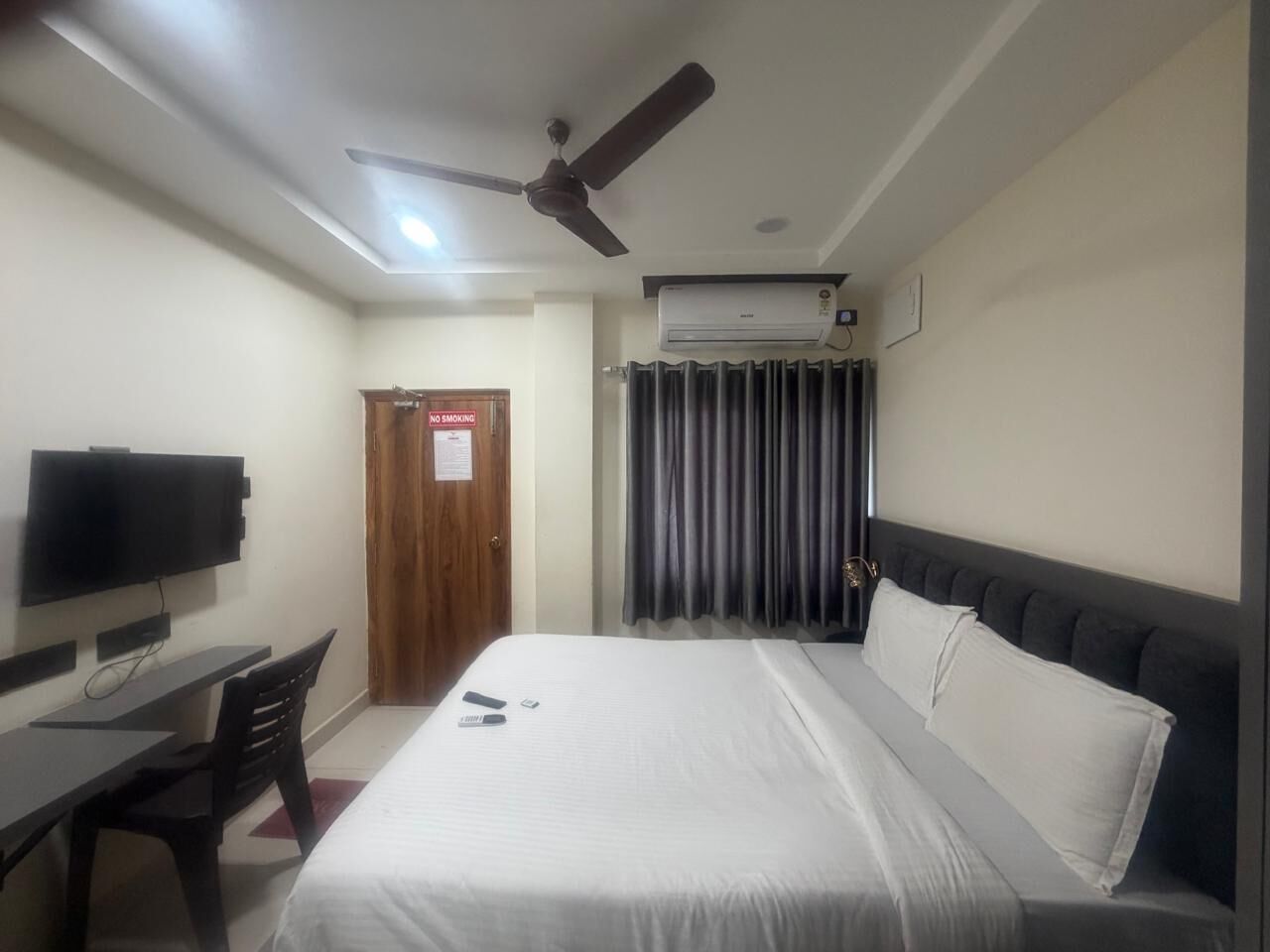 Ein Hotelzimmer mit Bett, Schreibtisch, Stuhl, Fernseher, Deckenventilator und Klimaanlage.