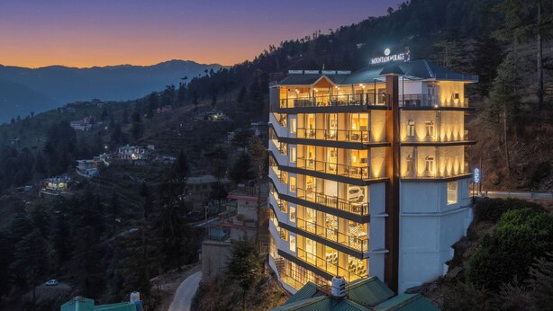 A multi-story hotel with balconies, located in a mountainous area with visible houses in the background. - HOTEL MOUNTAIN MIRAGE (Kumharsain)