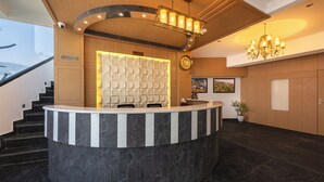 A reception area with a marble counter, a chandelier, a clock, and a staircase. - HOTEL MOUNTAIN MIRAGE (Kumharsain)