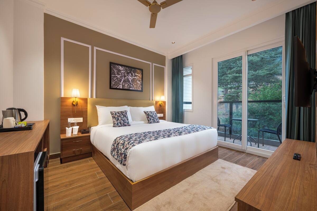 Une chambre dotée d’un grand lit, de lampes de chevet, d’un ventilateur de plafond, d’un tableau au mur et offrant une vue sur l’extérieur grâce à une porte-fenêtre coulissante.