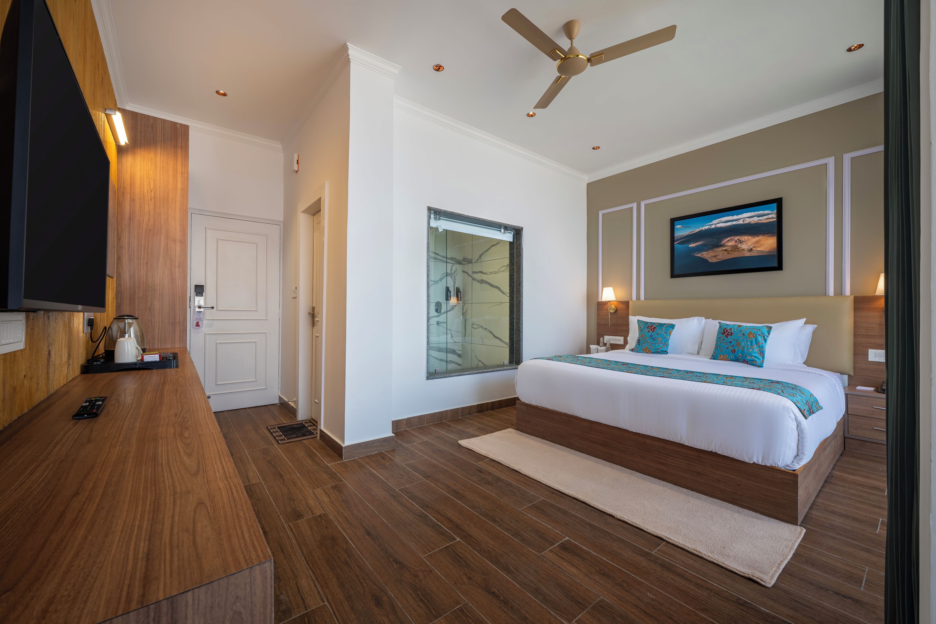Un dormitorio moderno con una cama grande, ventilador de techo, televisor y un cuadro en la pared.