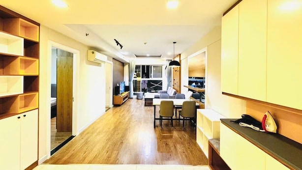 A modern kitchen with wooden cabinets, a dining area with a table and chairs, and a view into the living room. - Sunflower Home - Scenic Valley 2 (Ho Chi Minh City)