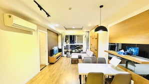 A modern living room with a sofa, dining table, and chairs, a TV, and a view through a large window. - Sunflower Home - Scenic Valley 2 (Ho Chi Minh City)