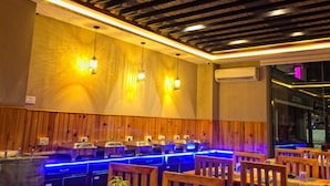 Un restaurante con paneles de madera, iluminación ambiental azul y lámparas colgantes.