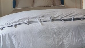Una cama con colcha a rayas, cabecera con paneles azules y grises, y una lámpara de noche.