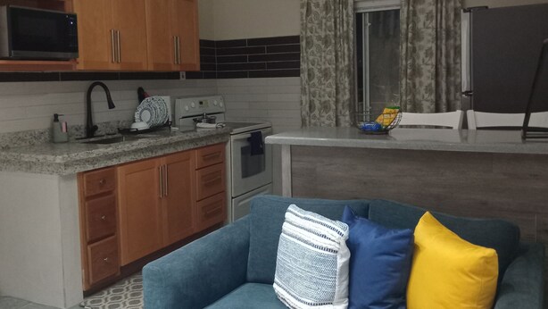 Una sala de estar con sofá, mesa de centro y una zona de cocina con armarios y electrodomésticos.