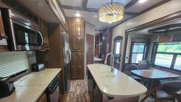 Une cuisine compacte pour camping-car, équipée d’un four à micro-ondes, d’une cuisinière et d’un évier, avec des placards en bois et un coin repas comprenant une table et des chaises.