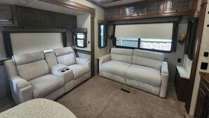 Un intérieur de camping-car compact comprenant deux canapés, un ventilateur de plafond et un coin cuisine avec des placards.