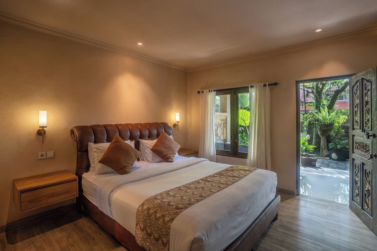 Quarto com cama grande, mesa de cabeceira, janela com cortinas e vista para o verde lá fora.